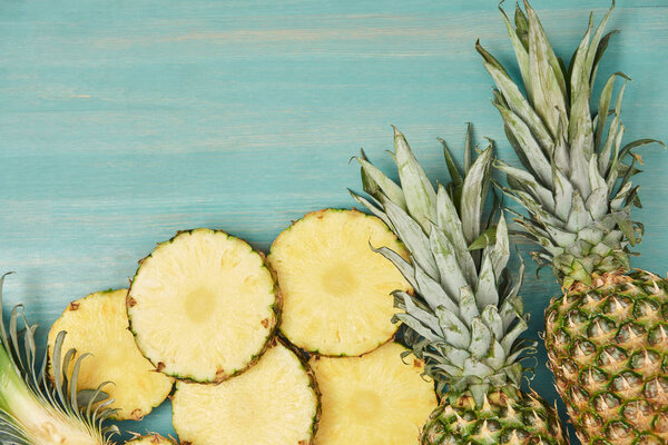 top view of sliced and whole pineapples on turquoise wooden table