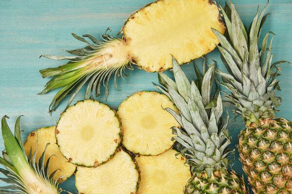 top view of whole and sliced pineapples on turquoise wooden table