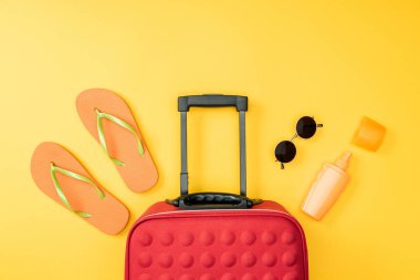 sarı arka plan üzerinde seyahat çantası, flip flop ve güneş gözlüğü üstten görünüm