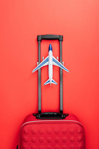 top view of travel bag with handle and toy plane on red background 