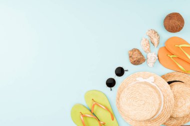 mavi arka plan üzerinde güneş gözlüğü, flip flop, hasır şapka ve deniz kabuklarını üstten görünüm 