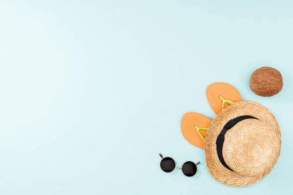 top view of sunglasses, flip flops, straw hat and coconut on blue background 
