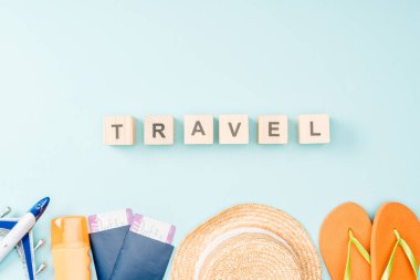 top view of wooden cubes with travel lettering, straw hat, flip flops, passports and air tickets on blue background clipart