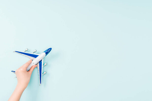 cropped view of woman holding small toy plane on blue background 