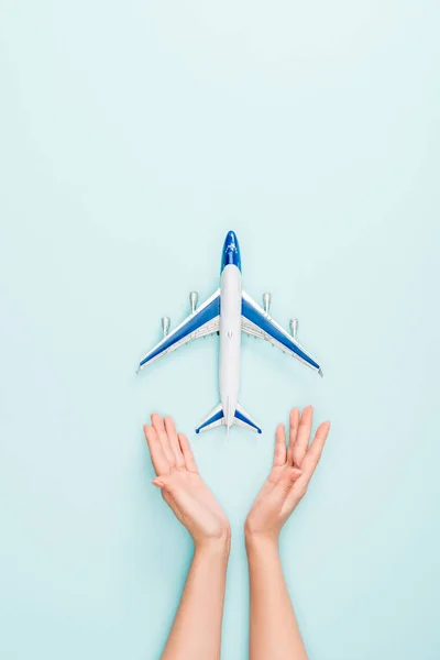 cropped view of woman holding hands near toy plane on blue background