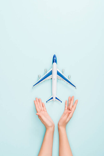 cropped view of woman holding hands near toy plane on blue background
