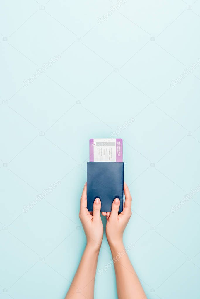 cropped view of woman holding passport with air ticket on blue background