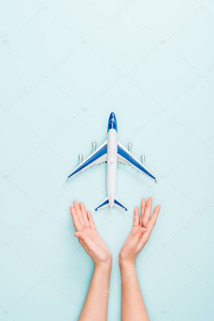 cropped view of woman holding hands near toy plane on blue background