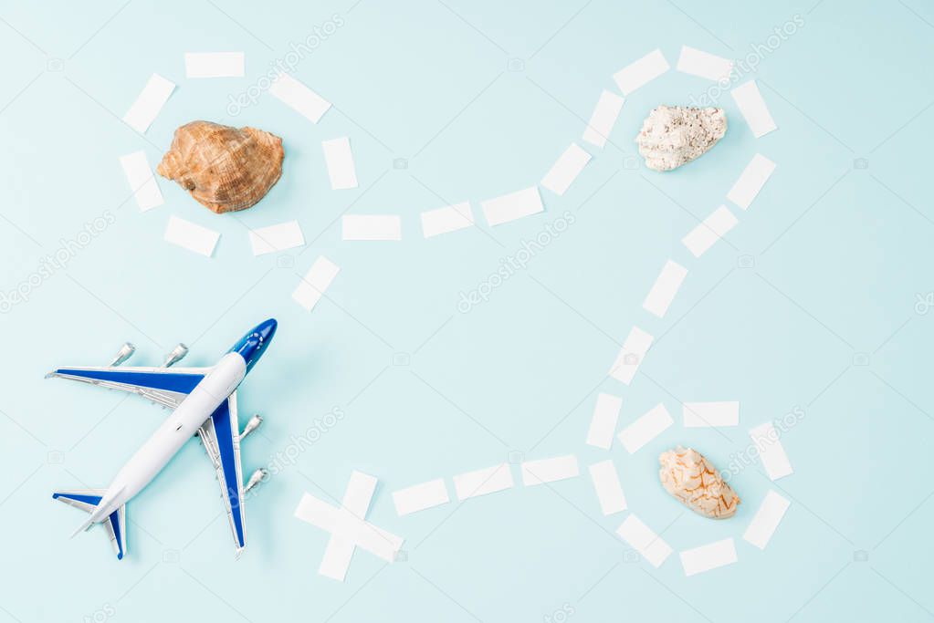 top view of toy plane, dotted line and seashells on blue background