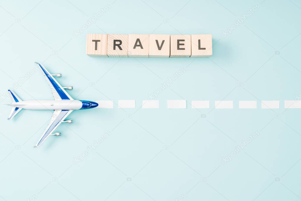 top view of toy plane, dotted line and wooden cubes with travel lettering on blue background