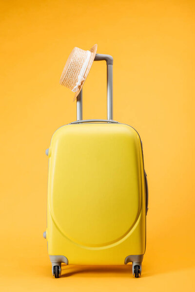 travel bag with wheels and straw hat on yellow background