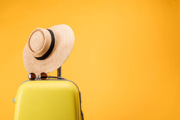 travel bag, straw hat and sunglasses isolated on yellow