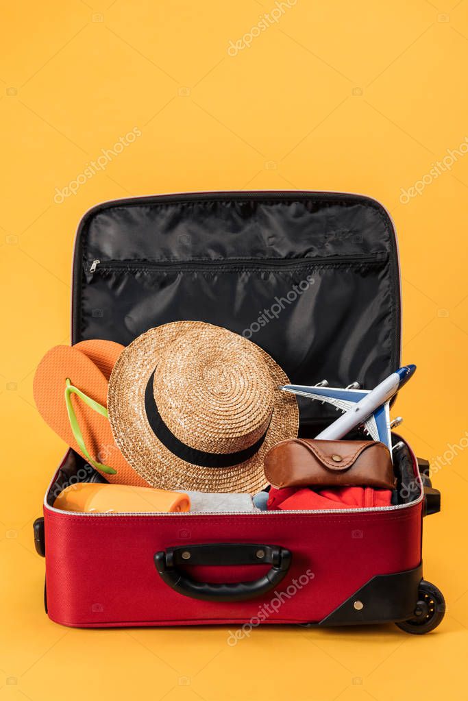 toy plane, straw hat, flip flops and clothes in travel bag on yellow background
