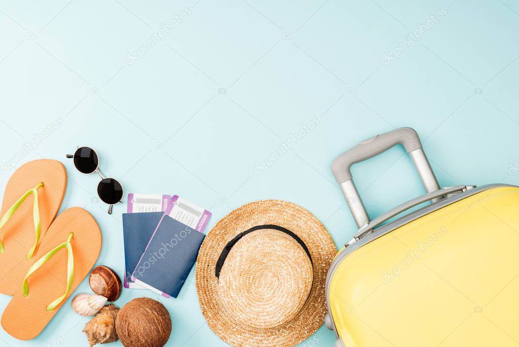 top view of straw hat, coconut, flip flops, seashells, sunglasses, passports, air tickets and travel bag on blue background