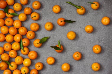top view of sweet orange tangerines with green leaves on grey table clipart