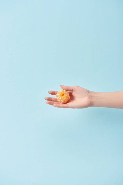 cropped view of woman holding peeled tangerine in hand isolated on blue 