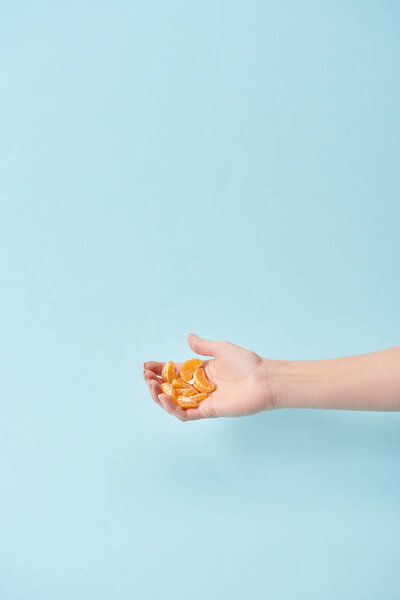 cropped view of woman holding slices of tasty peeled tangerine in hand isolated on blue 