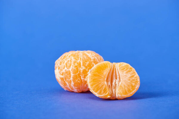 half of peeled tangerine near whole clementine on blue background 