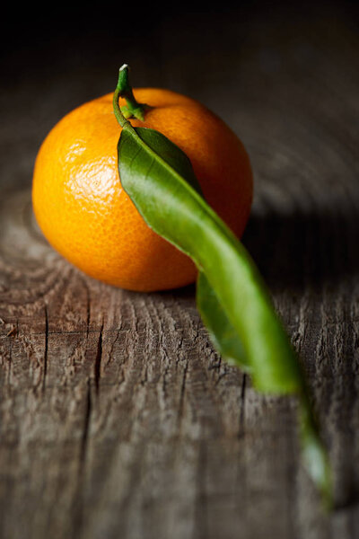 selective focus of juicy tangerine with green leaf on wooden table 