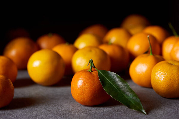 selective focus of orange clementine with green leaf near tangerines on grey table