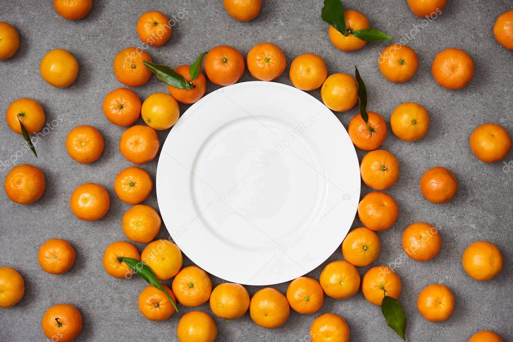 top view of fresh organic tangerines near white plate on grey table