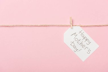 white paper label with happy mothers day greeting with coarse thread on pink background clipart