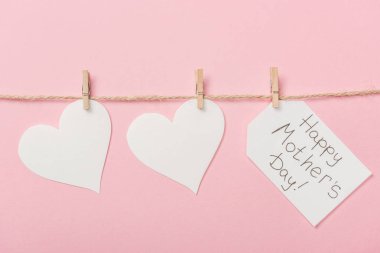 white paper hearts and label with happy mothers day greeting with coarse thread on pink background clipart