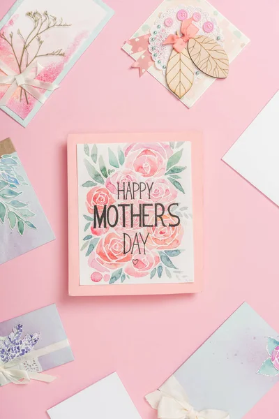happy mothers day greeting card with flowers, and various mothers day postcards arranged around on pink background