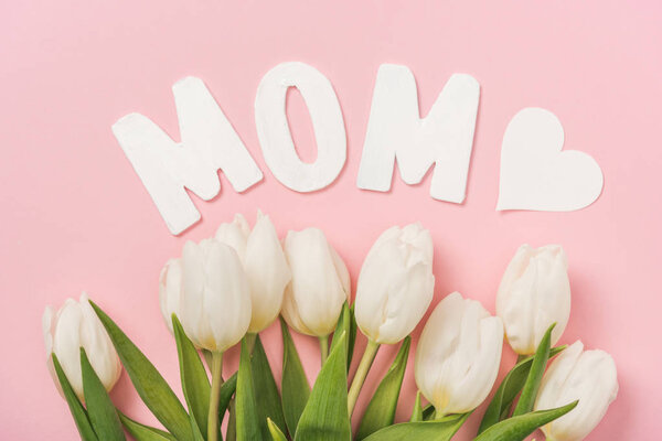 white tulips, paper word mom and paper hearts on pink background