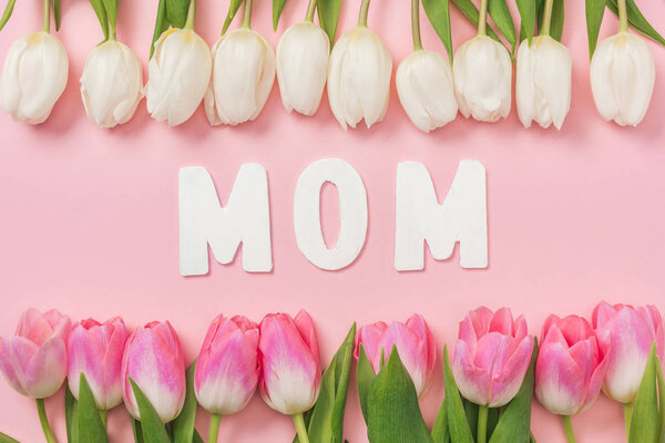 white and pink tulips arranged in rows and paper word mom on pink background