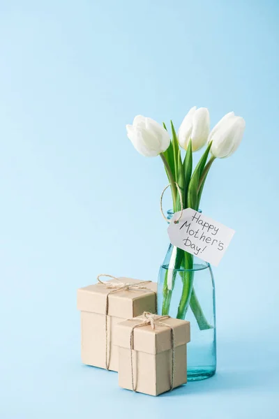 礼品盒和花束的白色郁金香与快乐的母亲天问候标签在蓝色背景 — 图库照片