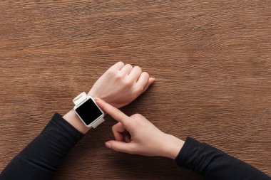 Cropped view of girl using smartwatch with blank screen on wooden background clipart