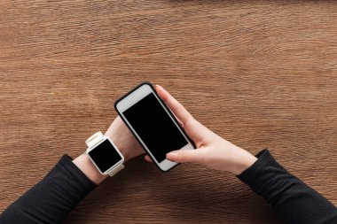 Boş ekran ile smartphone ile ahşap arka plan üzerinde tutarak smartwatch ile kız görünümünü kırpılmış