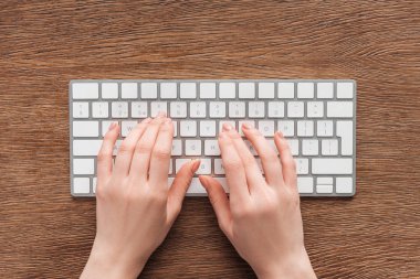 Partial view of woman typing on keyboard on wooden background clipart