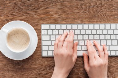 Cropped view of girl typing on keyboard on wooden background clipart