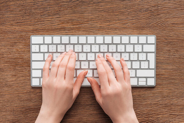 Частичное представление женщины, печатающей на клавиатуре на деревянном фоне
