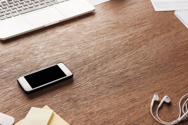Фото смартфона с чистым экраном и наушниками на деревянной поверхности

