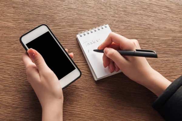 Cropped View Woman Holding Smartphone Blank Screen Writing Notebook — Stock Photo, Image