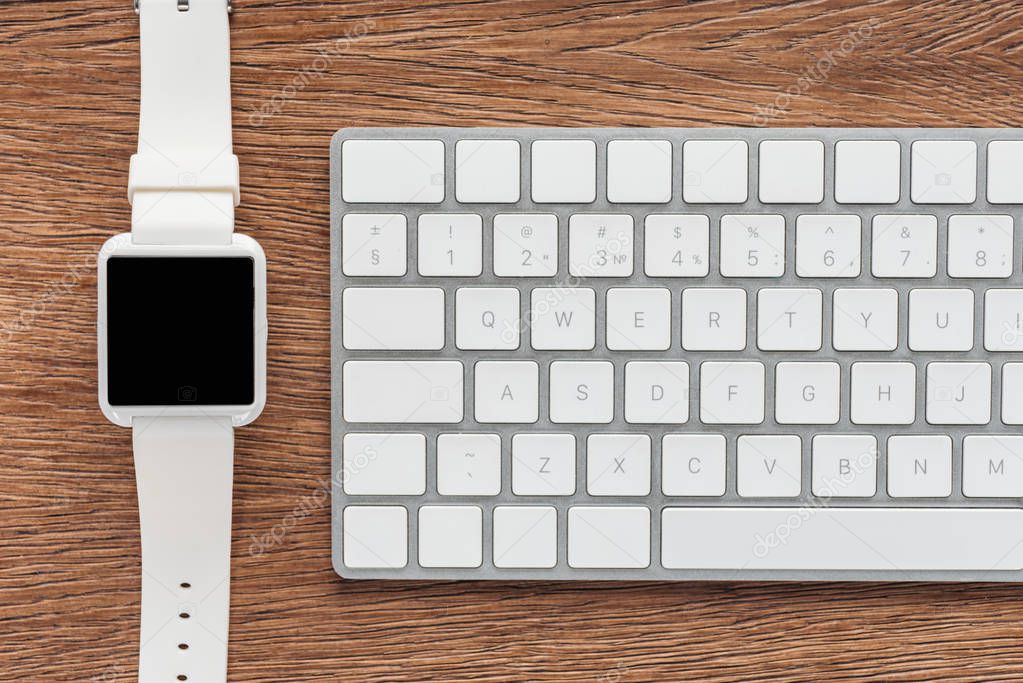 Top view of keyboard and smartwatch with blank screen on wooden background