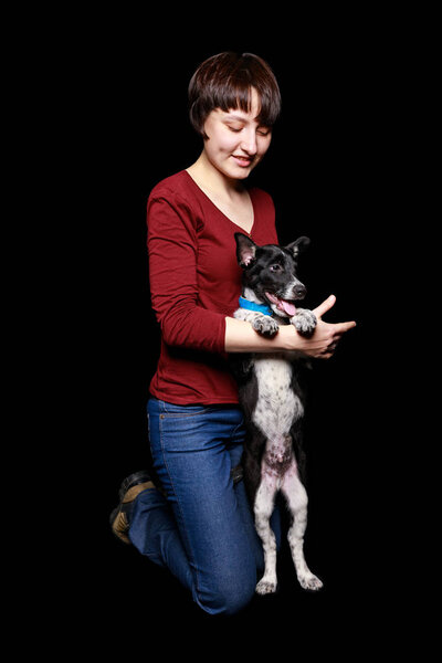 woman in jeans and red sweater with dog in collar on hind legs isolated on black