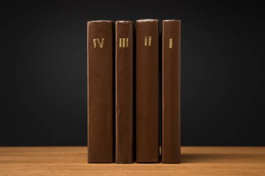 volumes of old books in leather brown covers on wooden table isolated on black clipart