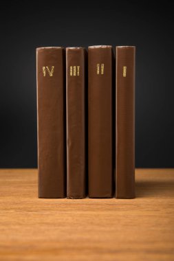 volumes of retro books in leather brown covers on wooden table isolated on black clipart