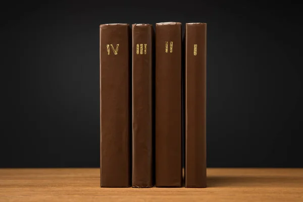 volumes of old books in leather brown covers on wooden table isolated on black