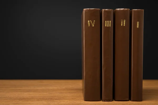 volumes of vintage books in leather brown covers on wooden table isolated on black