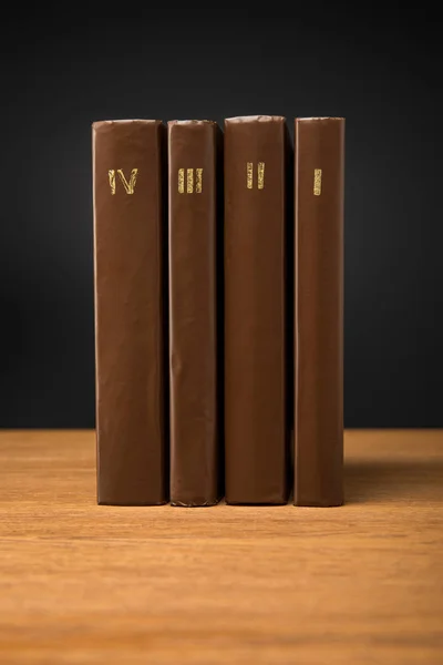 volumes of retro books in leather brown covers on wooden table isolated on black