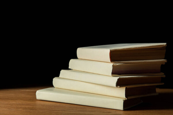 pile of books in white covers on wooden table isolated on black