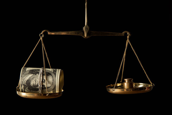 cash roll of dollar banknotes on vintage golden scales isolated on black