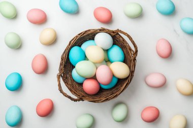 Beyaz üzerinde dağınık pastel Paskalya yumurtaları ve hasır sepet Üstten Görünüm 