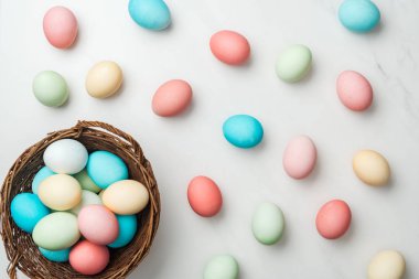 Beyaz üzerinde dağınık pastel Paskalya yumurtaları ve hasır sepet Üstten Görünüm 