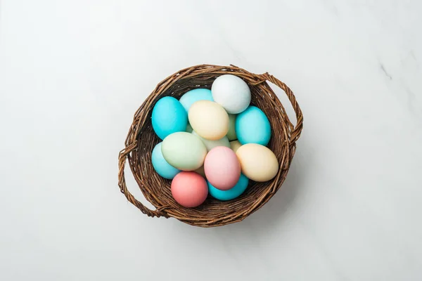 在白色柳条篮子里的五颜六色的粉彩复活节彩蛋的顶部视图 — 图库照片